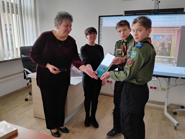 Harcerze wręczają prezent pracownikom biblioteki.