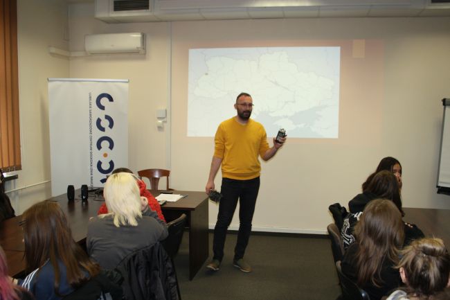 Łukasz Kot z dyktafonem w ręku opowiada młodzieży o pracy dziennikarza.