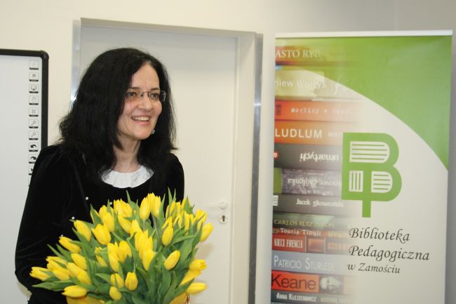Prof. Sabina Bober stoi uśmiechnięta z bukietem kwiatów na zakończenie spotkania autorskiego.